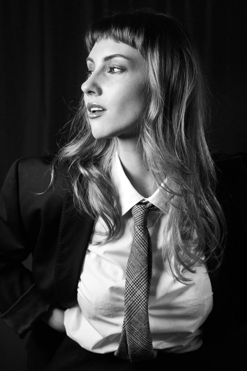 Woman with a fringe, white shirt and tie looking aside in black and white