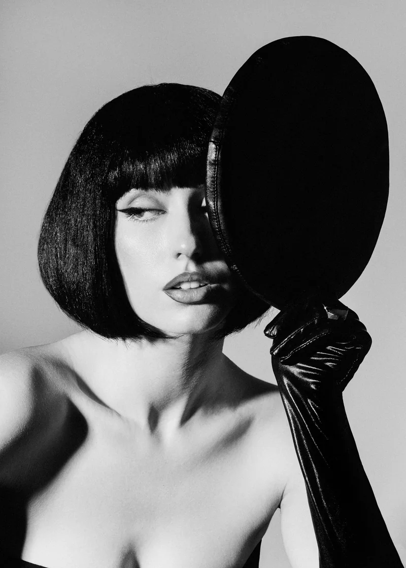 Woman with a glossy black bob and a long glove covering half of her face with a black beret