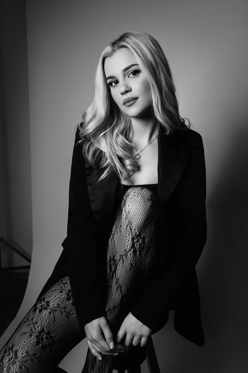Blonde woman in a black blazer seated in black and white studio light