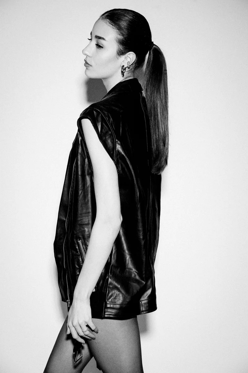 Woman with a ponytail in a black leather vest turned in profile
