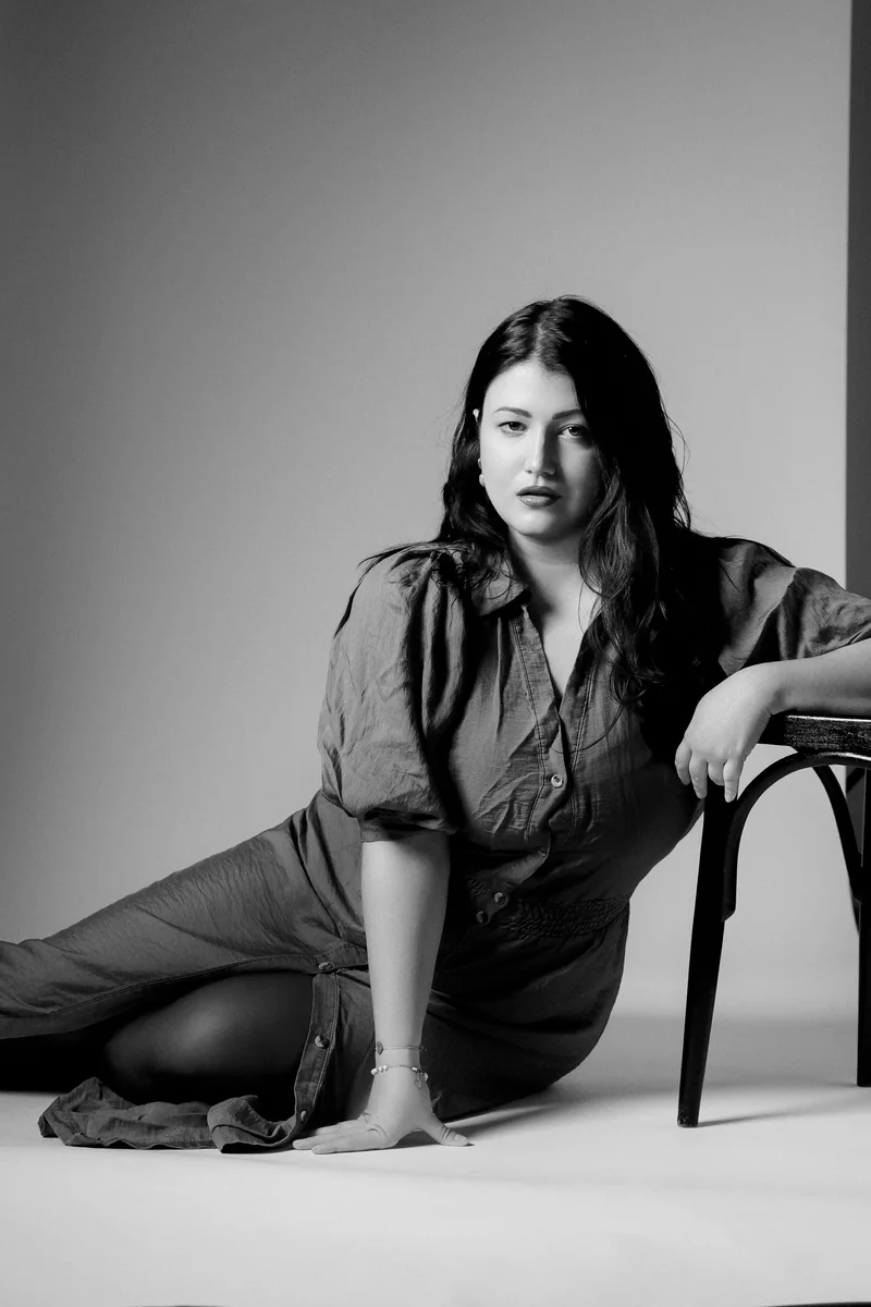 Woman in a dark jumpsuit sitting on the floor and leaning against a chair