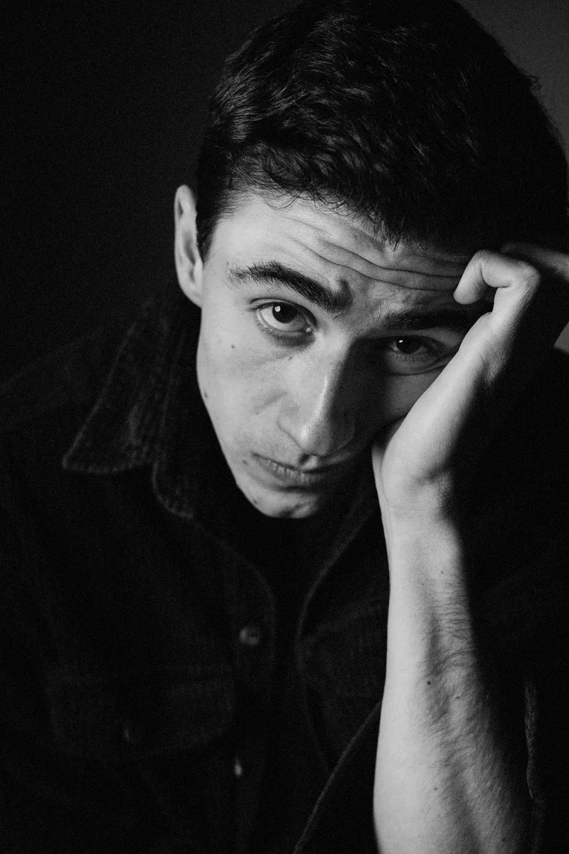 Man resting his head on his hand, looking into the camera in low light