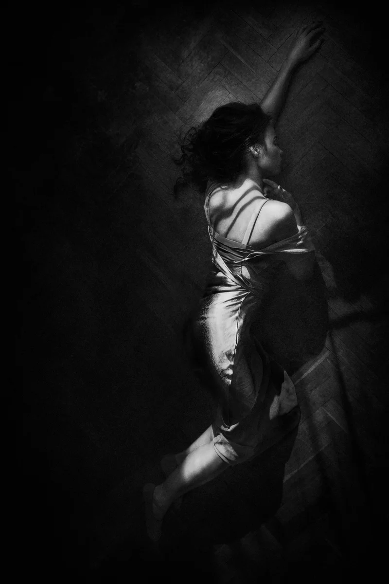 Woman in a satin slip dress lying on a parquet floor with one arm outstretched, seen from above