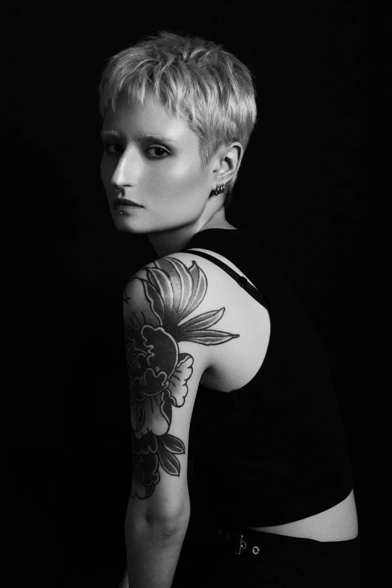 Woman with short bleached hair and a large floral tattoo on her arm