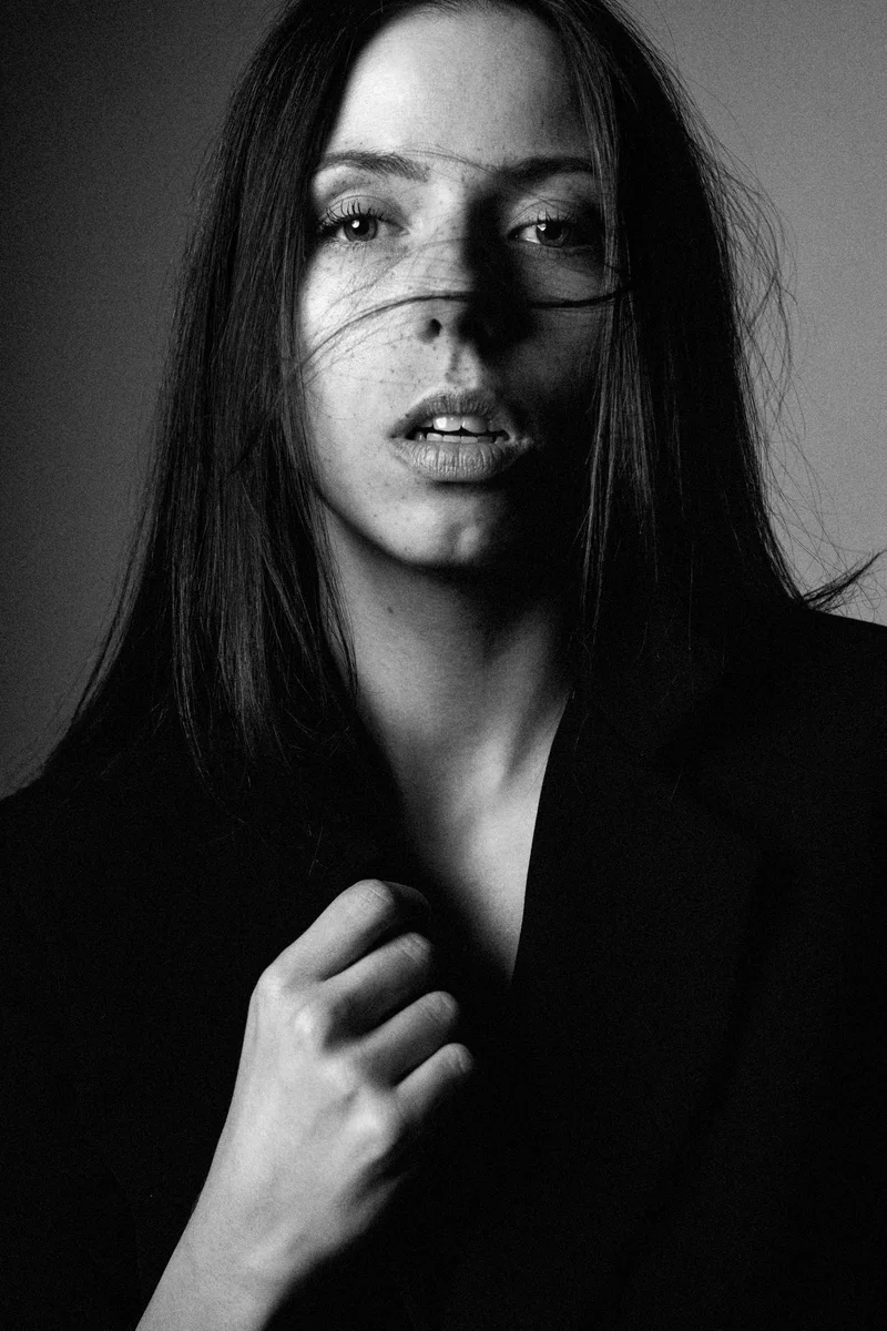 Woman in a black blazer with hair across her face and a hand on the lapel