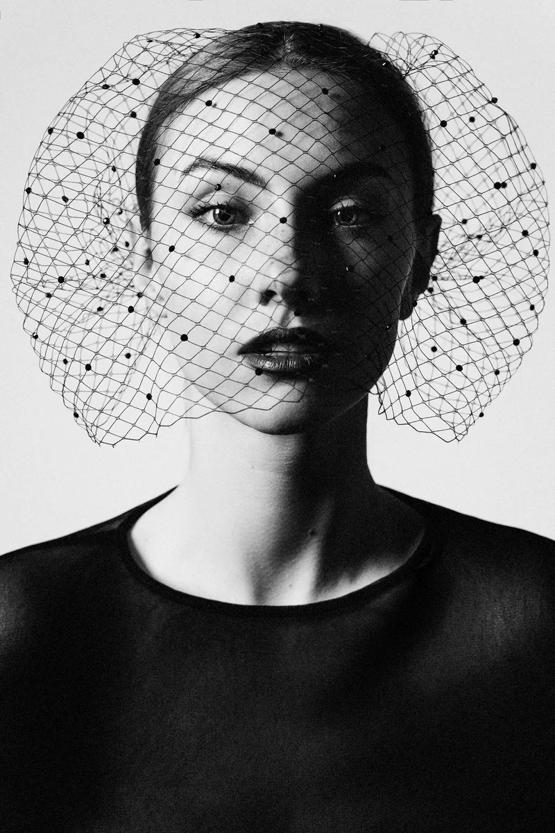 Frontal black and white portrait of a woman in a round net veil