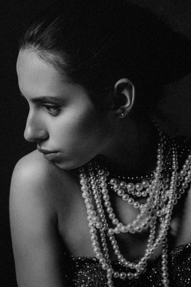 Woman with swept-back hair and layers of pearl necklaces looking down in profile