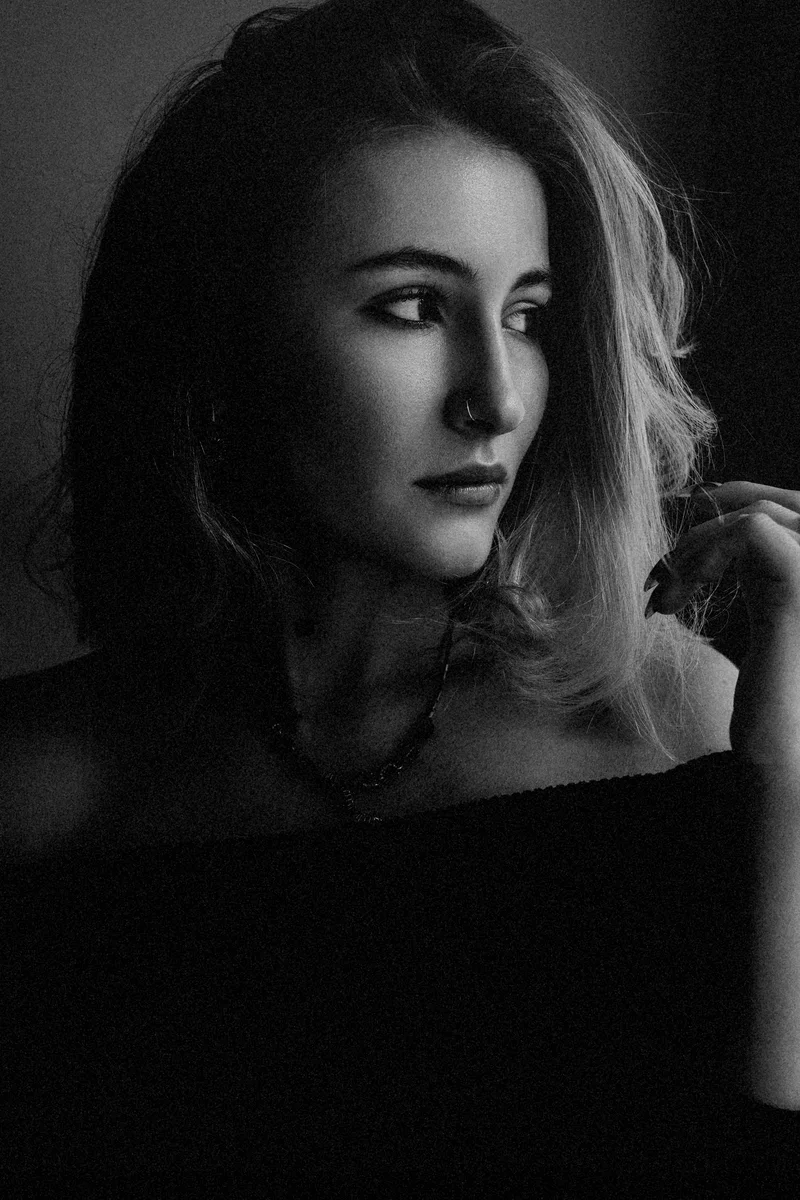 Woman with wavy hair and a bare shoulder looking right in deep shadow
