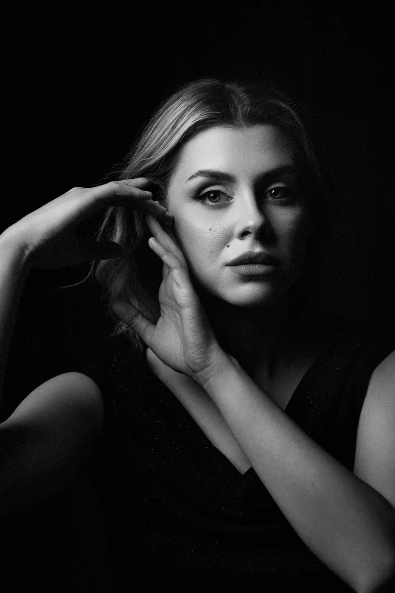 Blonde woman with a hand in her hair, in a black top and side light
