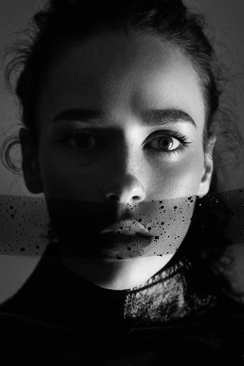 Woman with spotted black tulle across her mouth, her face half in shadow