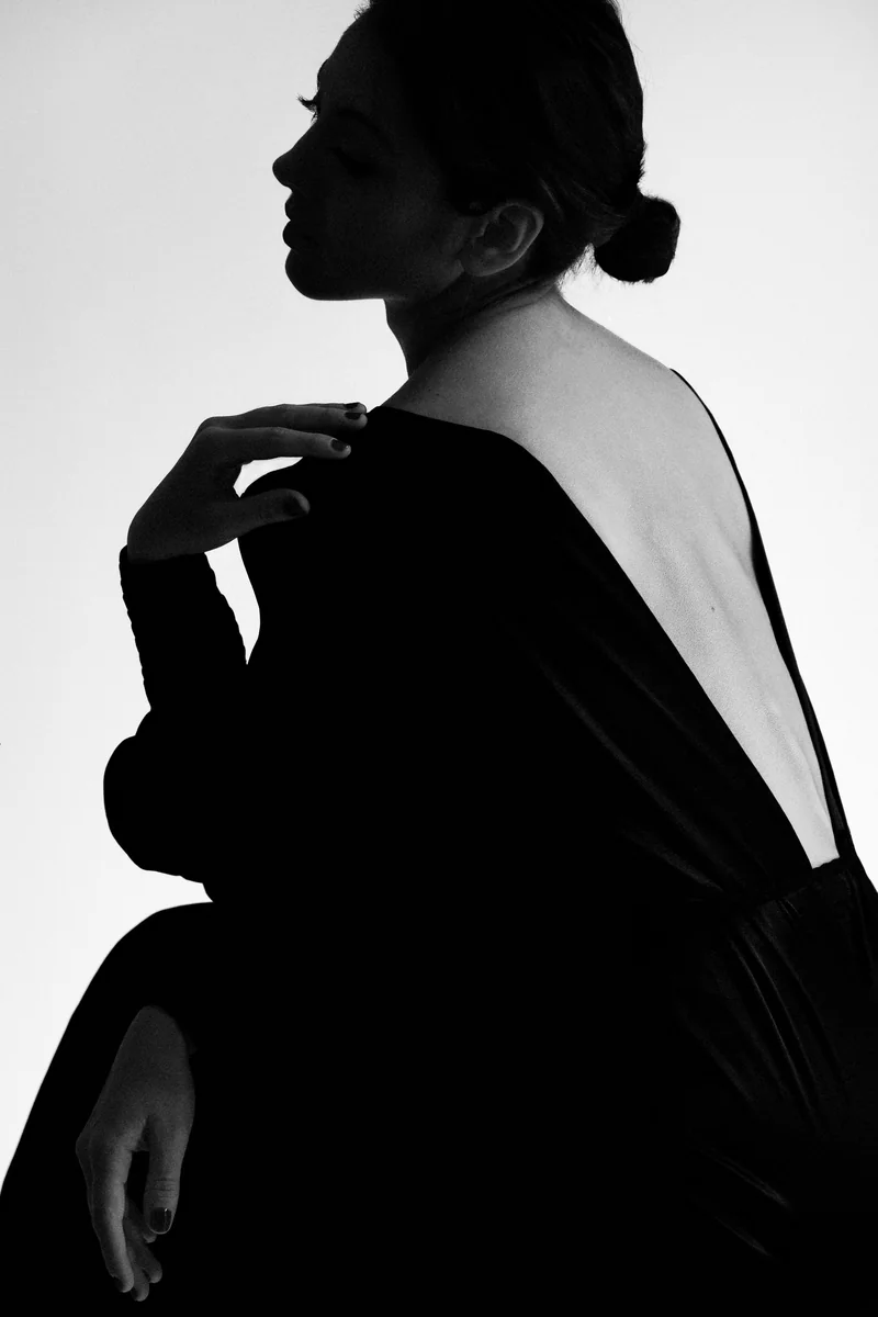 Woman in profile with her hair in a bun and a black open-back dress against white