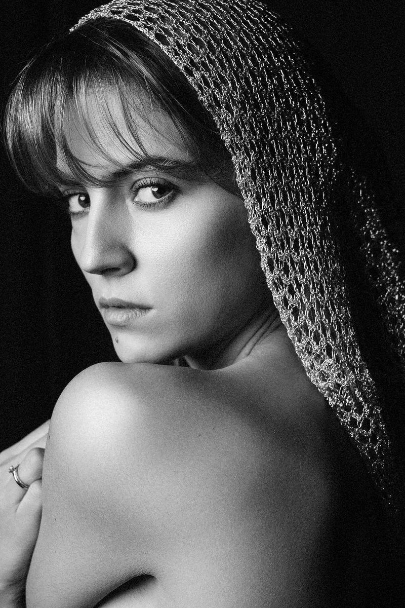 Woman with a fringe and a knitted headscarf looking over her bare shoulder