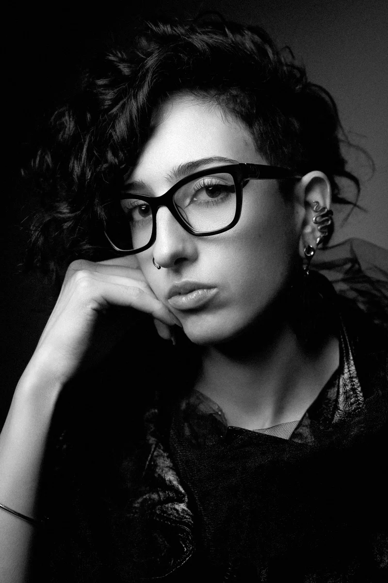 Woman with short curly hair and glasses resting her head on her hand