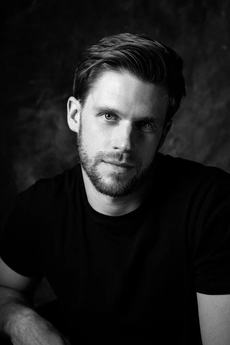 Bearded man in a black T-shirt leaning forward in black and white light