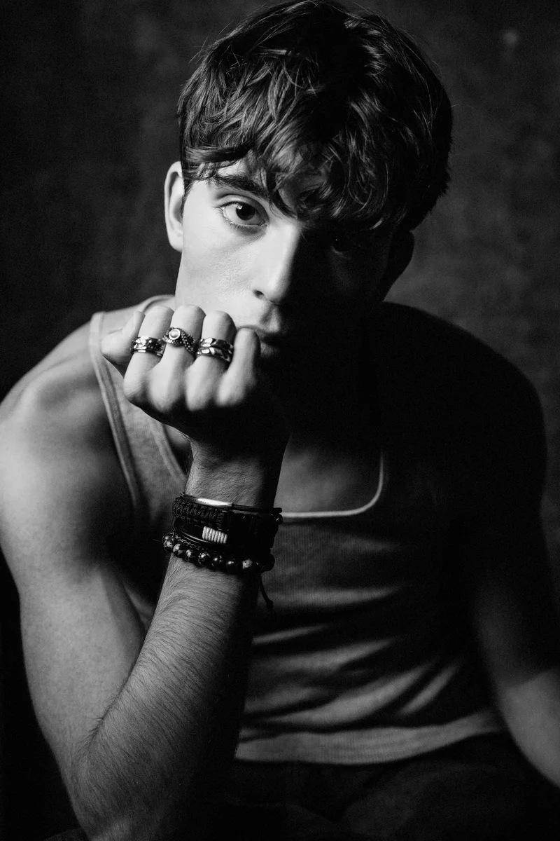 Portrait with a grey vest, short hair and rings on a hand held beside the lips