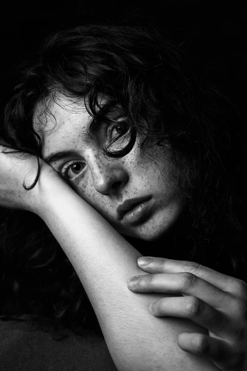 Curly-haired freckled woman resting her face against a raised arm