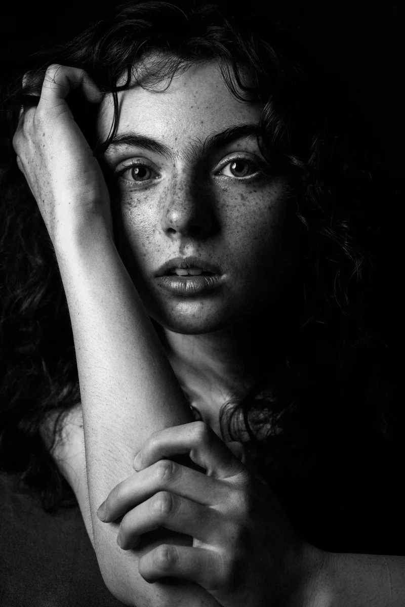 Curly-haired freckled woman raising an arm above her head in black and white