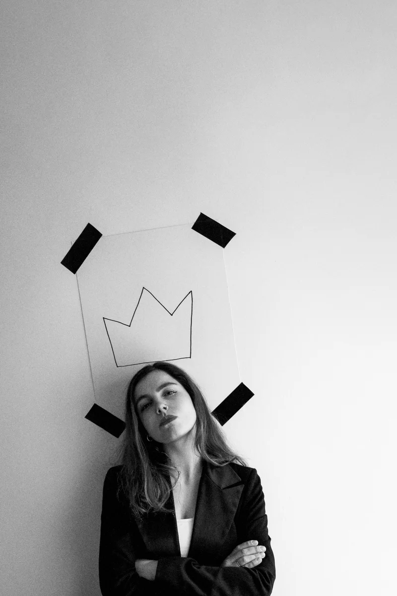 Woman in a black blazer standing beneath a drawn crown held up with black tape