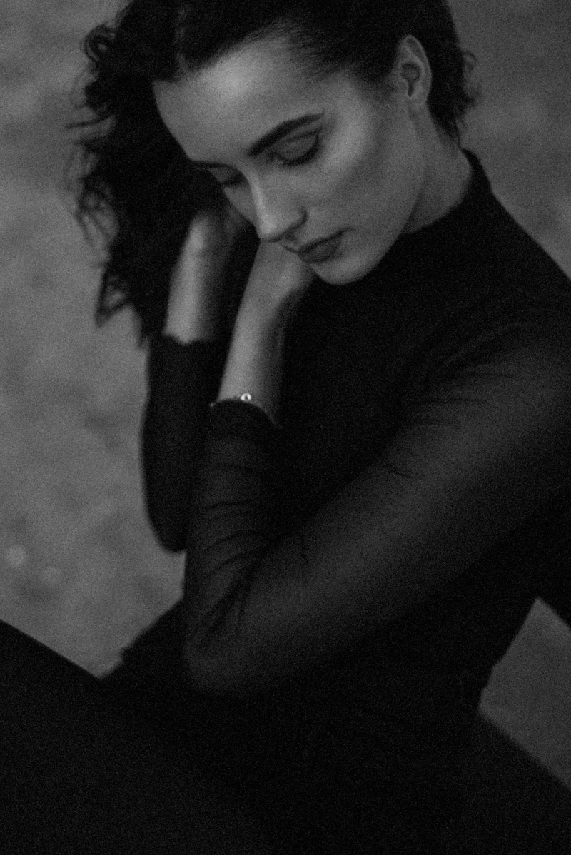 Woman with dark hair in a black top, her head bowed and a hand at her neck