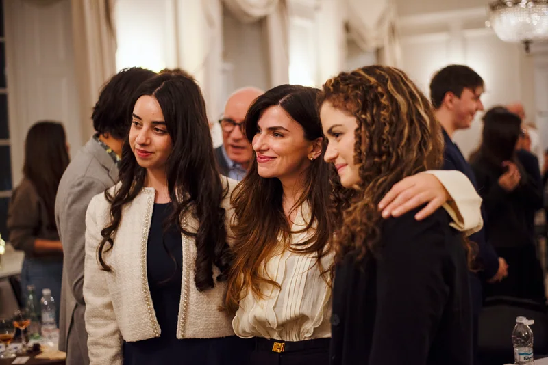 Three smiling women posing arm in arm at an evening reception