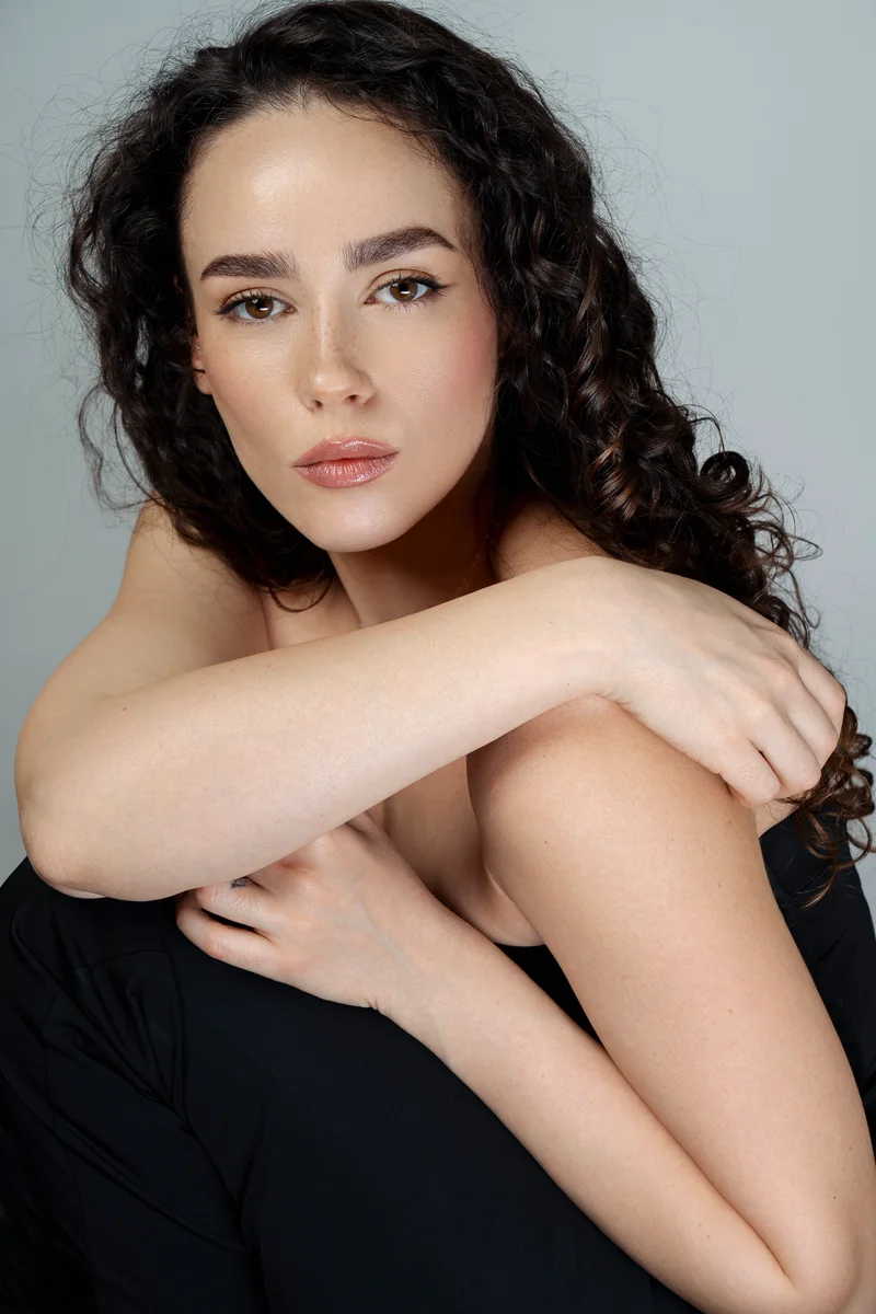 Woman with long curly hair in a black top, her arm across her shoulder