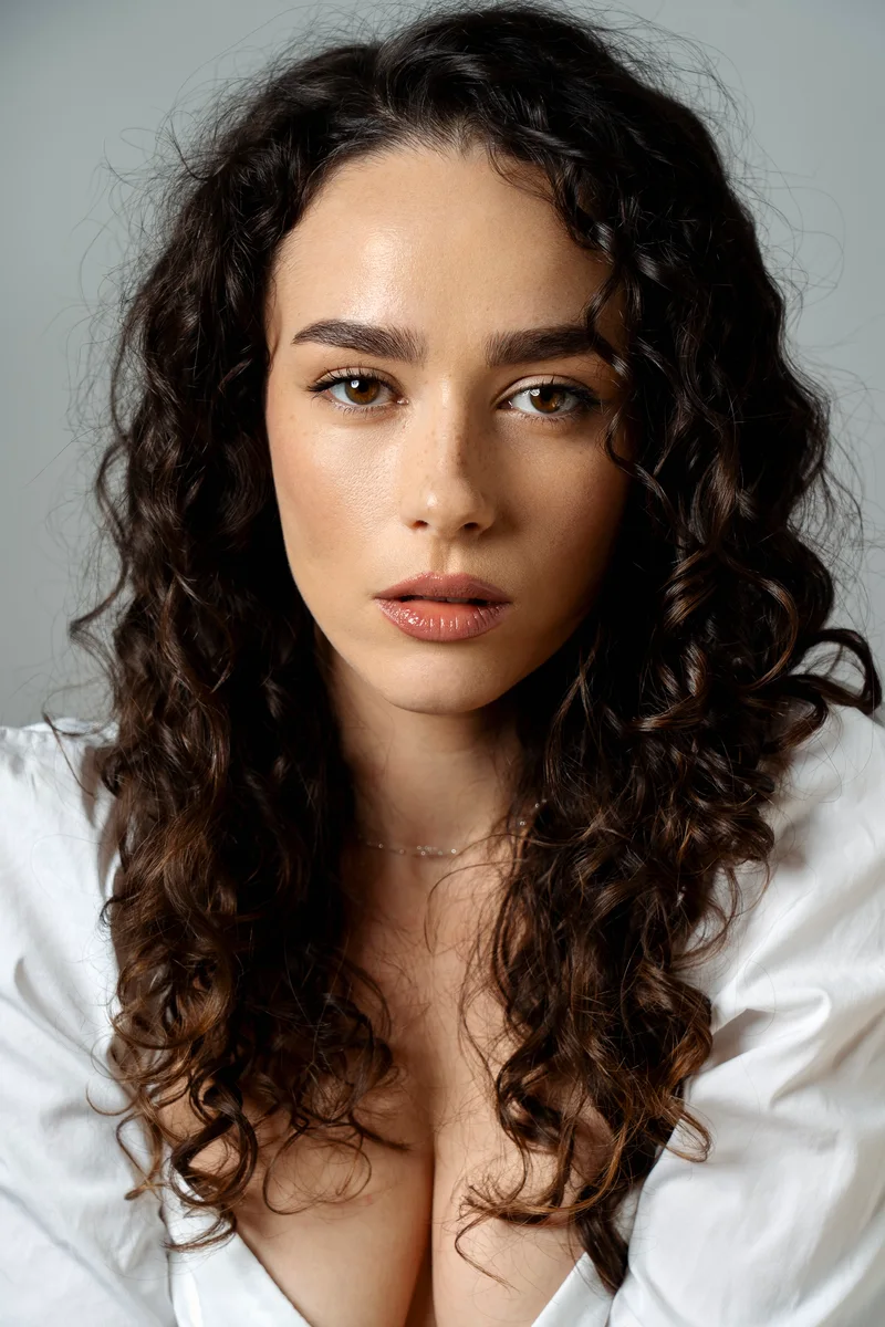 Woman with long curly hair in a white shirt looking into the camera
