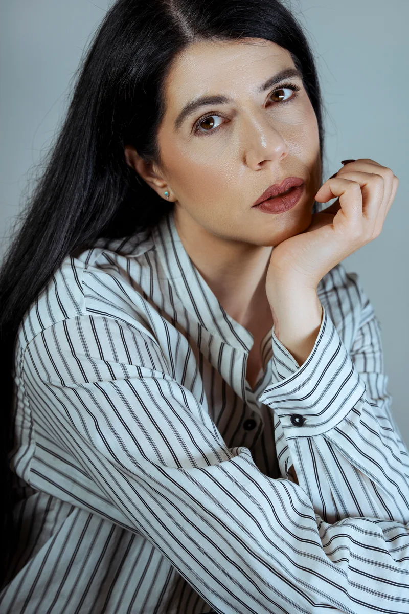 Woman with long black hair in a striped shirt, resting her chin on her hand