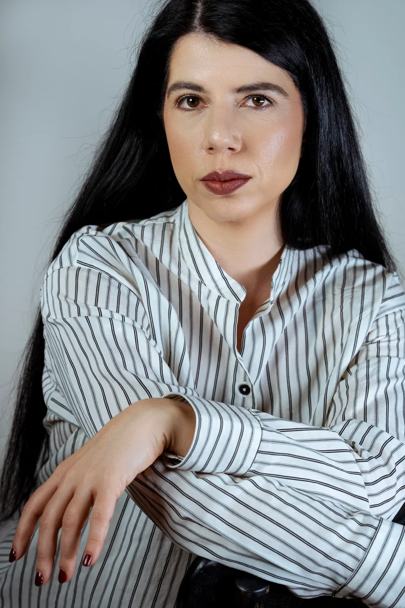Woman with long black hair in a striped shirt, arms crossed in front of her