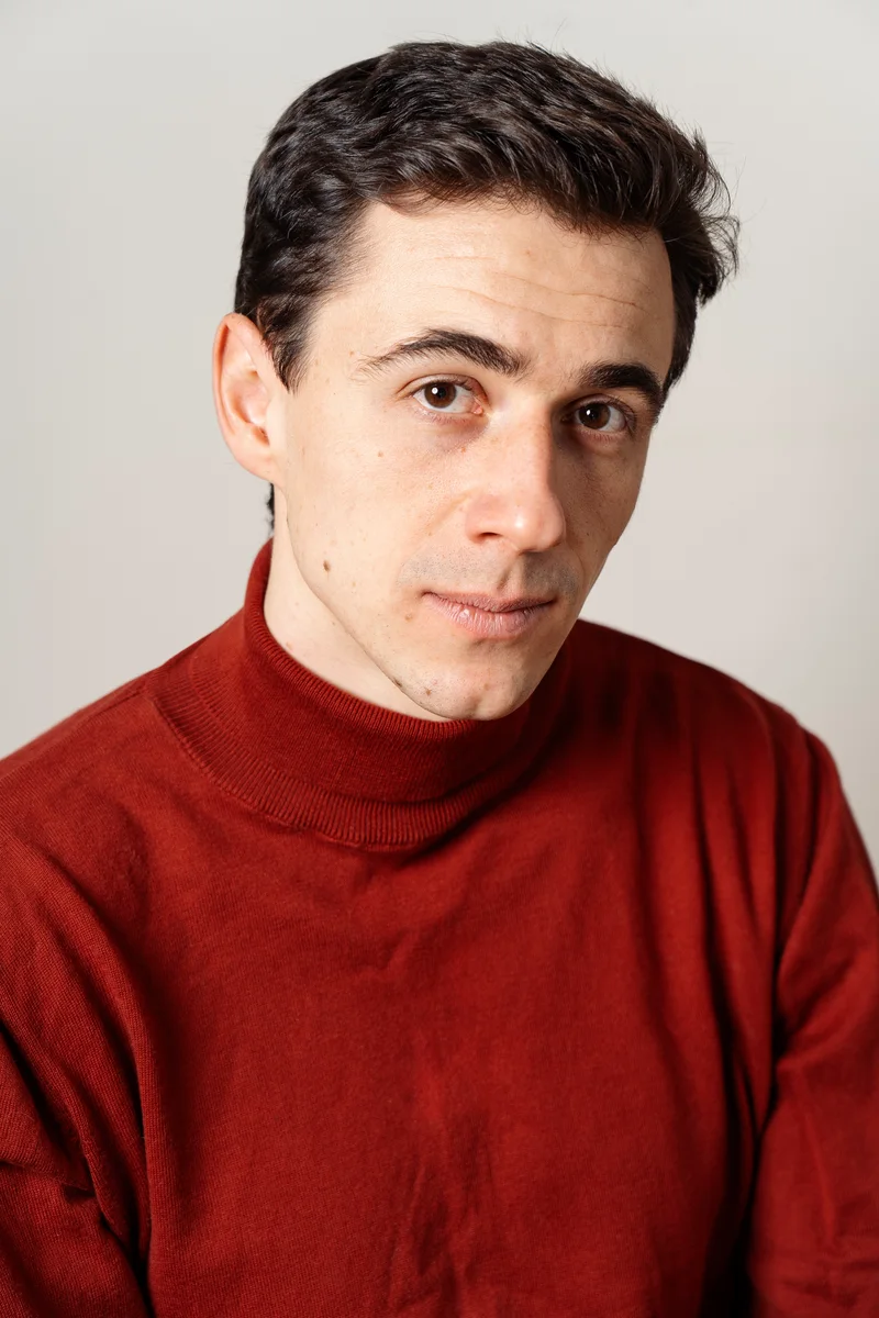 Dark-haired man in a red turtleneck against a light background