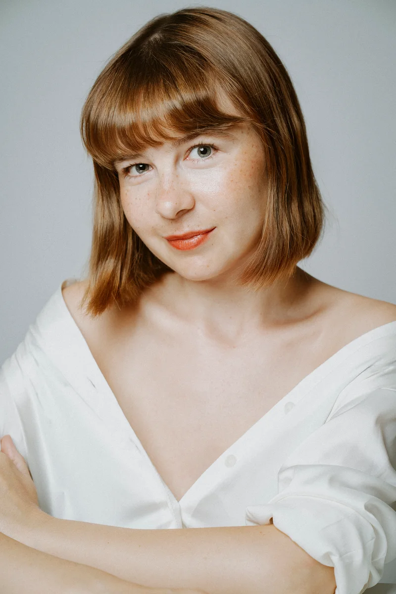 Woman with a short auburn bob in a white shirt sitting with her arms folded