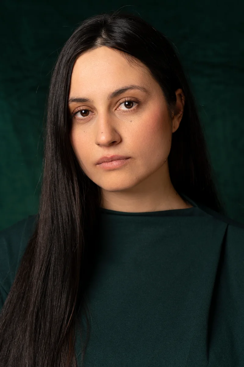 Woman with long straight dark hair in a dark green top against green