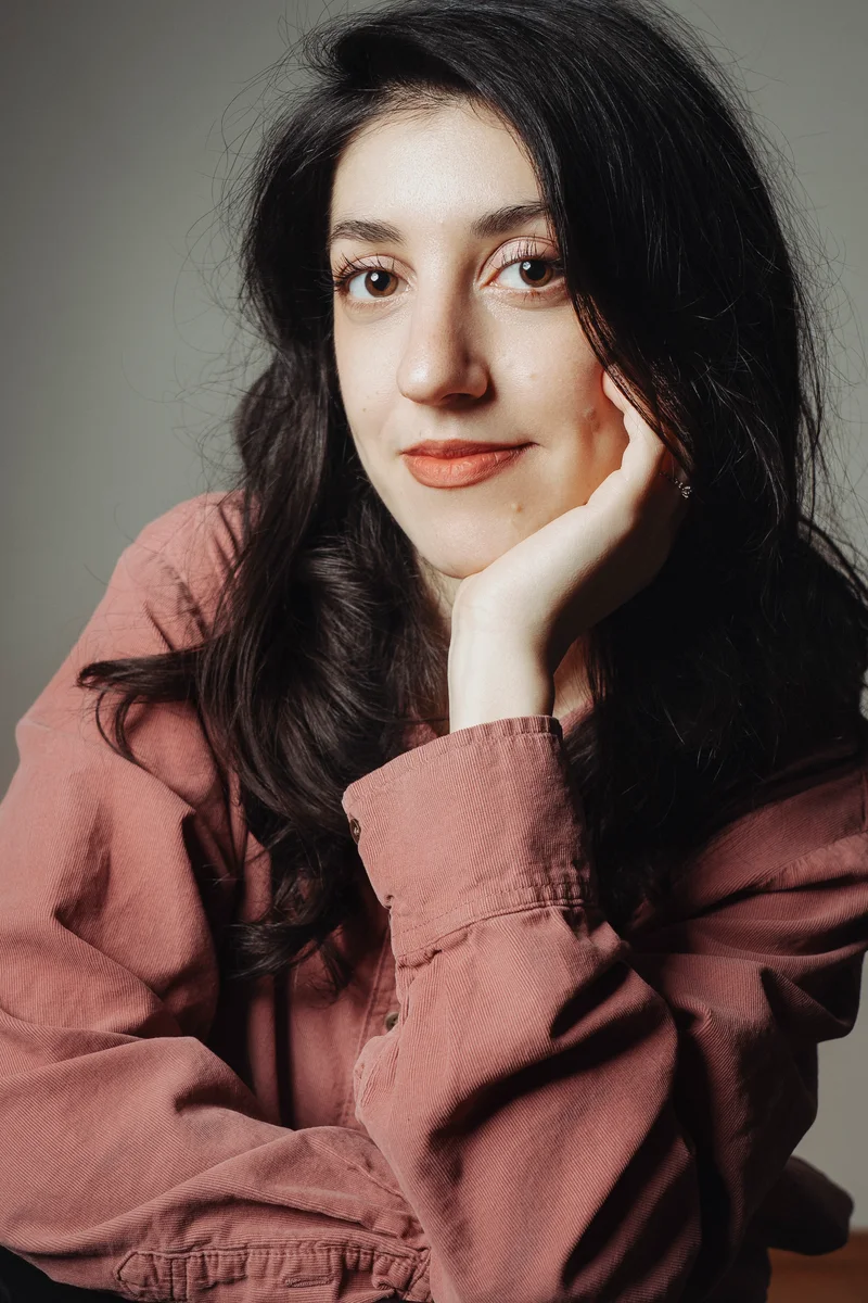 Woman with long dark hair in a pink shirt resting her cheek on her hand