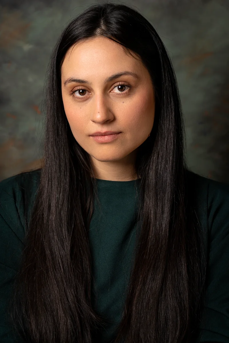 Woman with long dark hair in a green top against a mottled grey-green backdrop