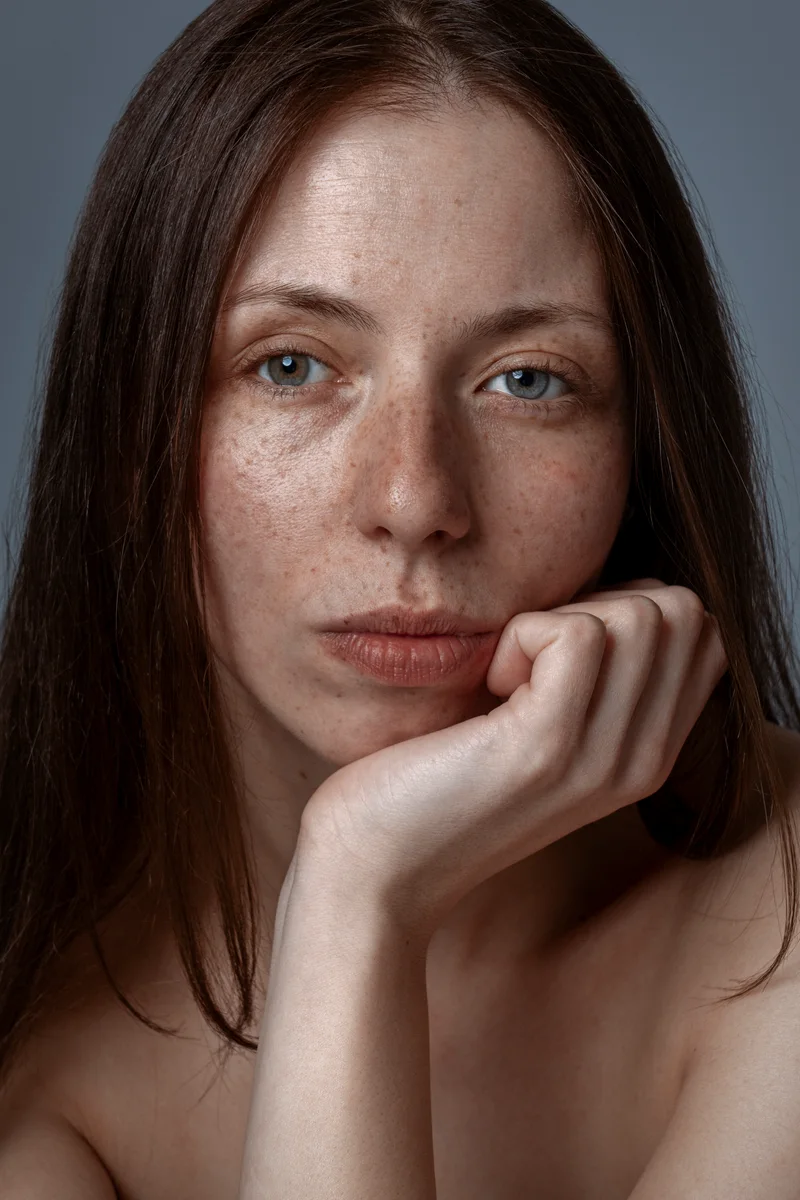 Freckled woman with long auburn hair resting her chin on her hand