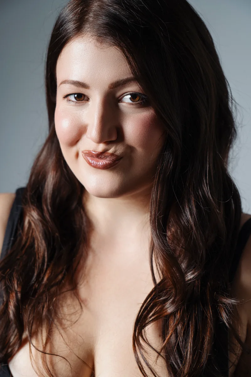 Woman with long brown hair and a slight smile against a pale backdrop