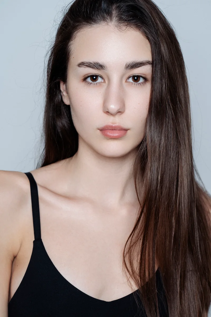Woman with long straight hair and a black vest in a simple frontal portrait