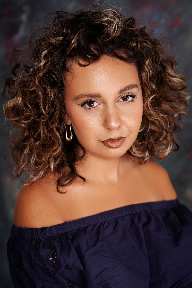 Woman with short curls in a dark blue top with bare shoulders