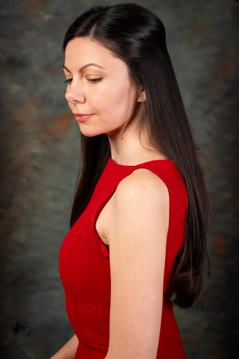 Woman with long dark hair in a red dress, in profile, looking down