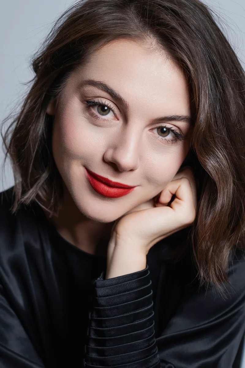 Smiling woman with red lipstick and a black top resting her face on her hand