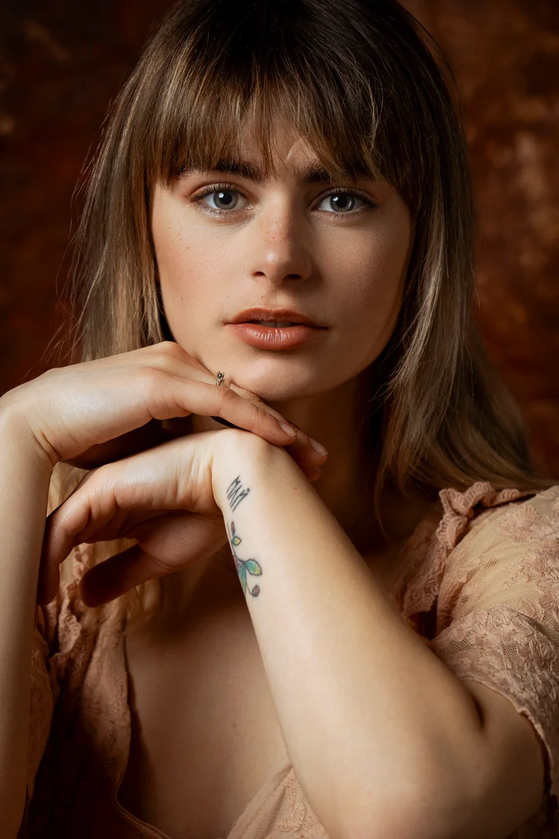 Woman with a fringe resting her chin on her hands against a rust-coloured backdrop