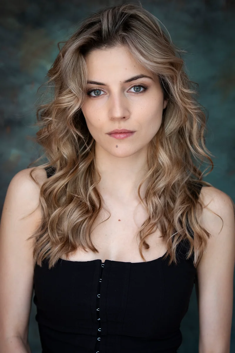 Woman with long blonde waves in a black top against a textured backdrop