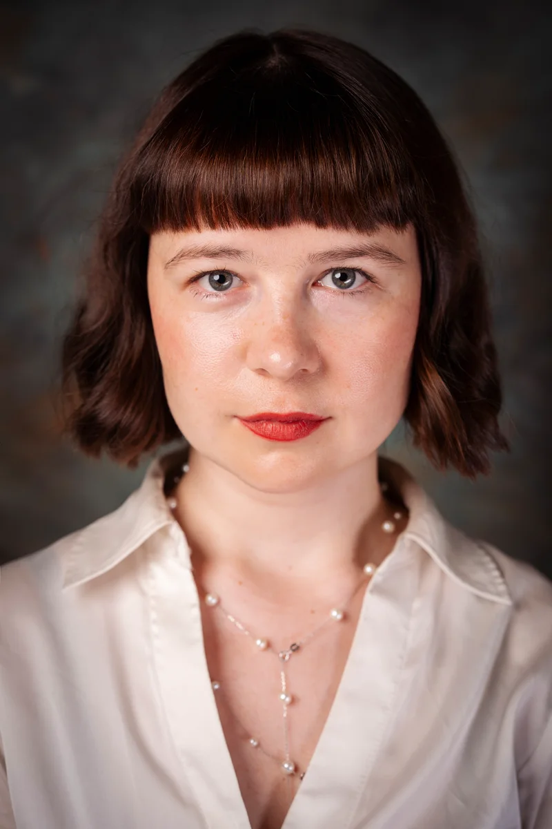 Woman with a dark fringed bob, red lipstick and a satin blouse
