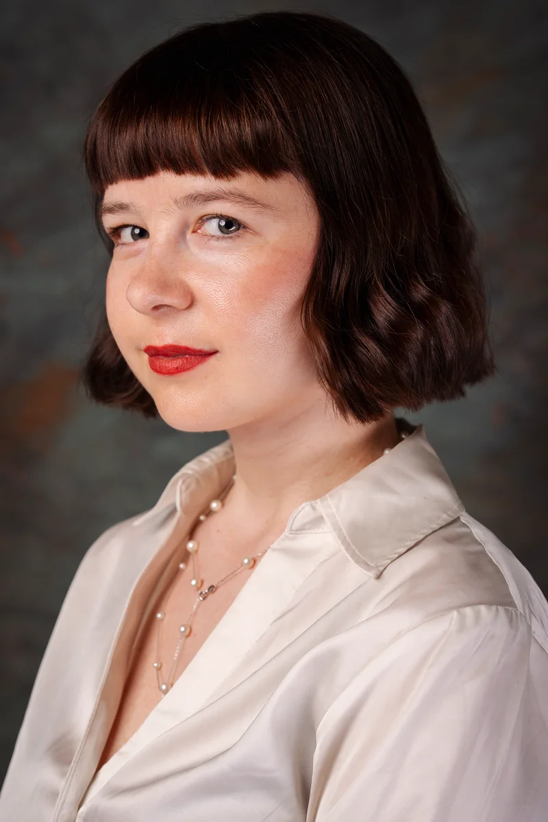 Woman with a fringed bob and a pearl necklace glancing over her shoulder