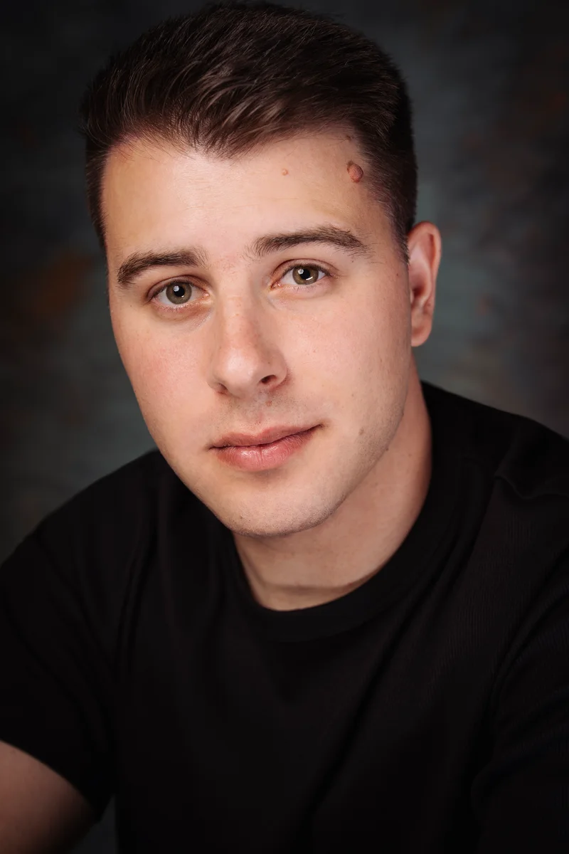 Man with short dark hair in a black T-shirt looking straight into the camera