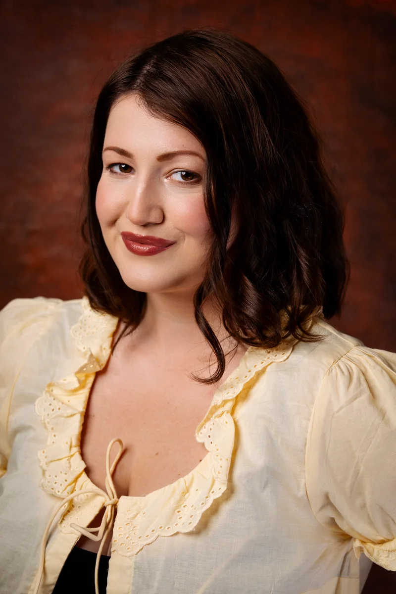 Smiling woman with dark hair in a yellow ruffled blouse against rust