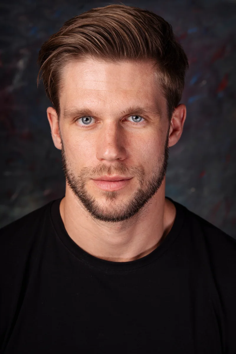Man with a short beard and black T-shirt looking ahead against a dark studio backdrop