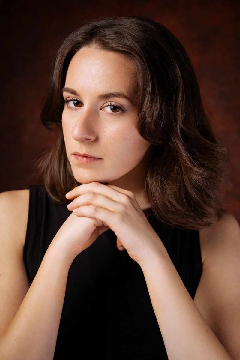 Woman with wavy brown hair in a black top, her chin resting on her hands