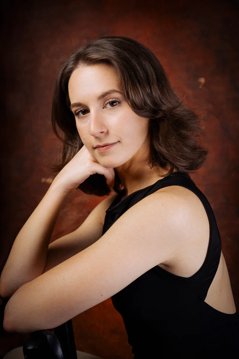 Woman in a black top sitting sideways on a chair against rust