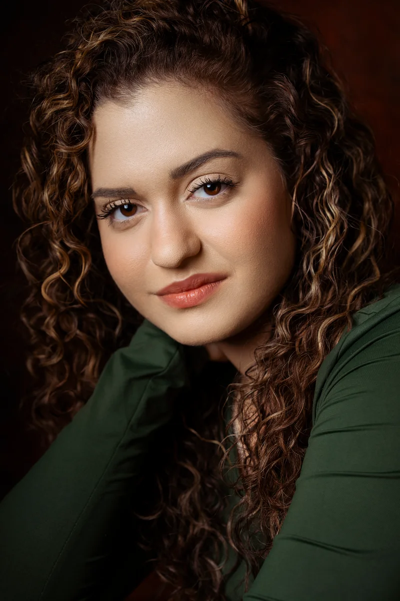 Woman with long curly hair in a green top leaning slightly forward