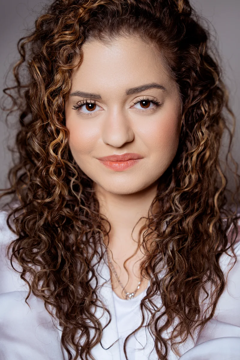Woman with long curls and a white shirt in a softly lit studio portrait